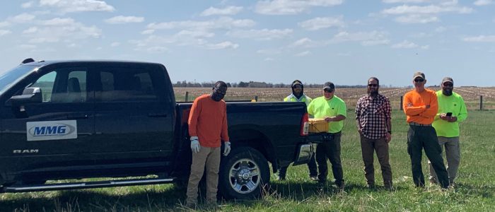 A work crew gathered around a RAM pickup truck with an MMG sign/logo on the side of the truck